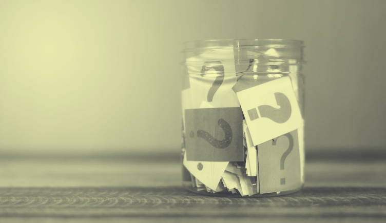 A glass jar filled with papers that have question marks on them.