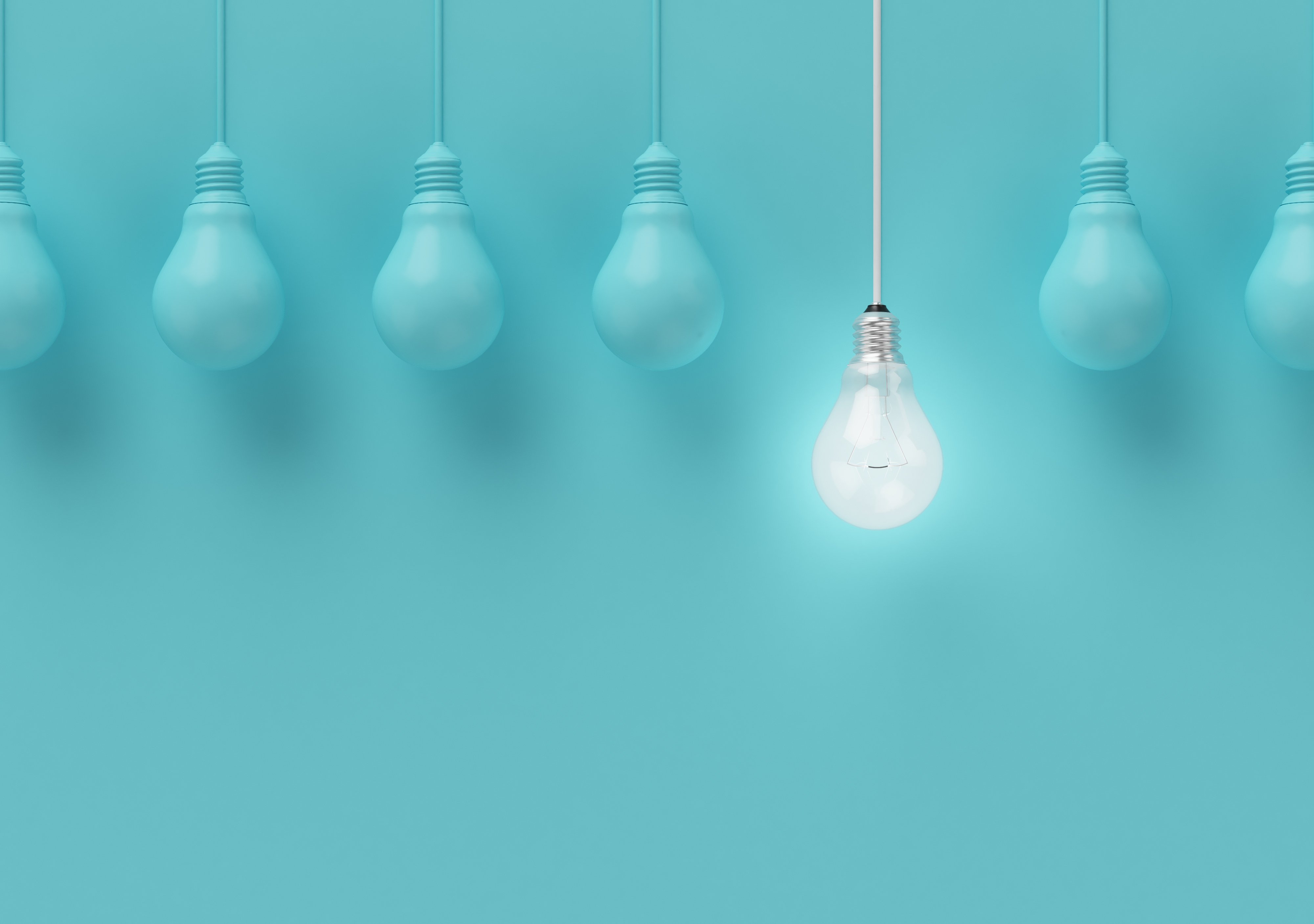 Image of a lightbulbs hanging in a row. Only one is illuminated and the rest are covered in blue paint to match the background behind them.