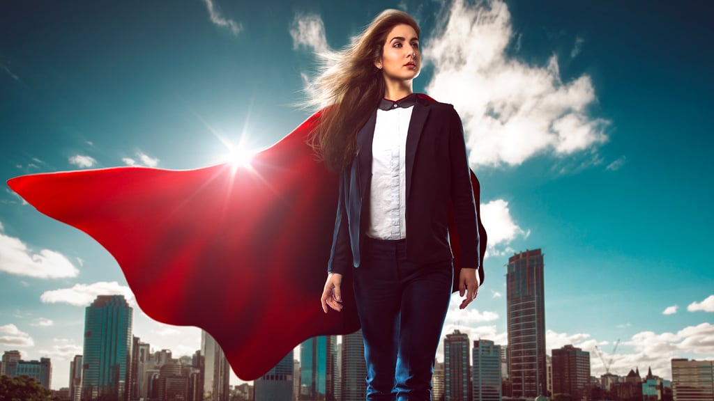 Successful businesswoman wearing a red superhero cape with a city skyline in the background