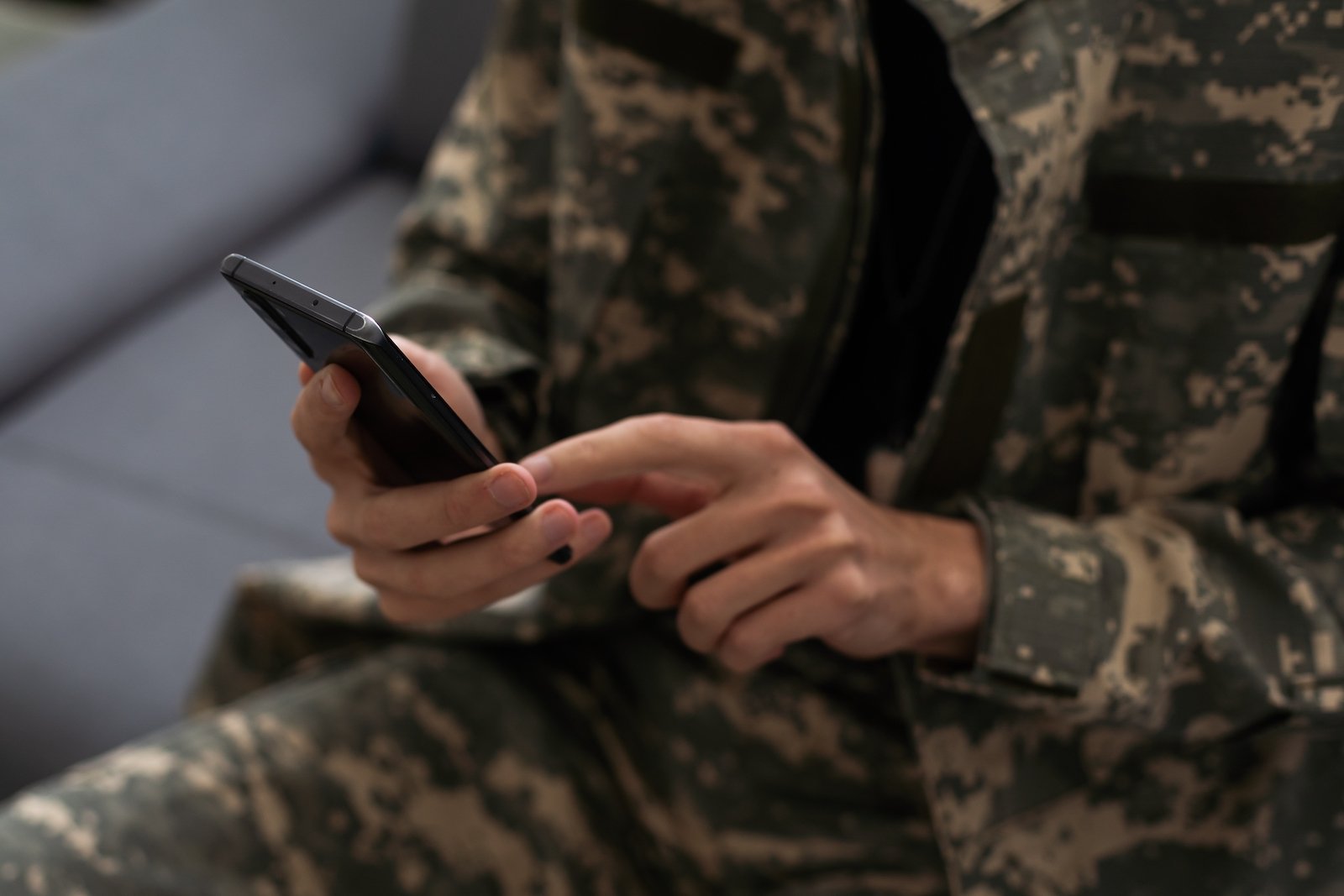 A person in army fatigues holding a cellphone.