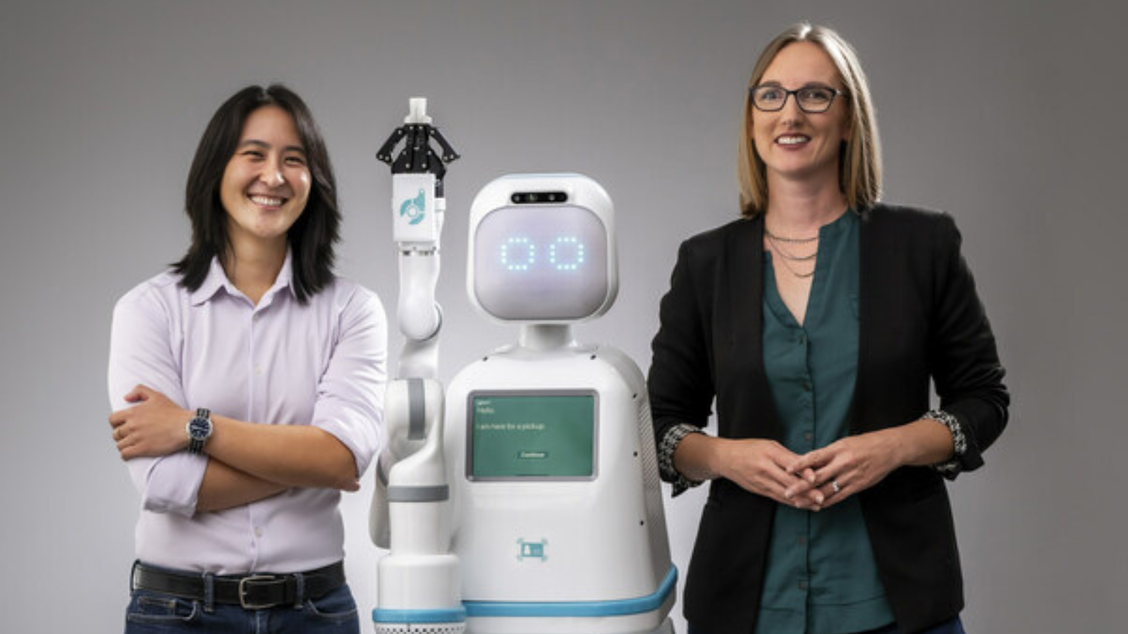 Dr. Andrea Thomaz and Dr. Vivian Chu from Diligent Robotics stand on either side of the Moxi robot