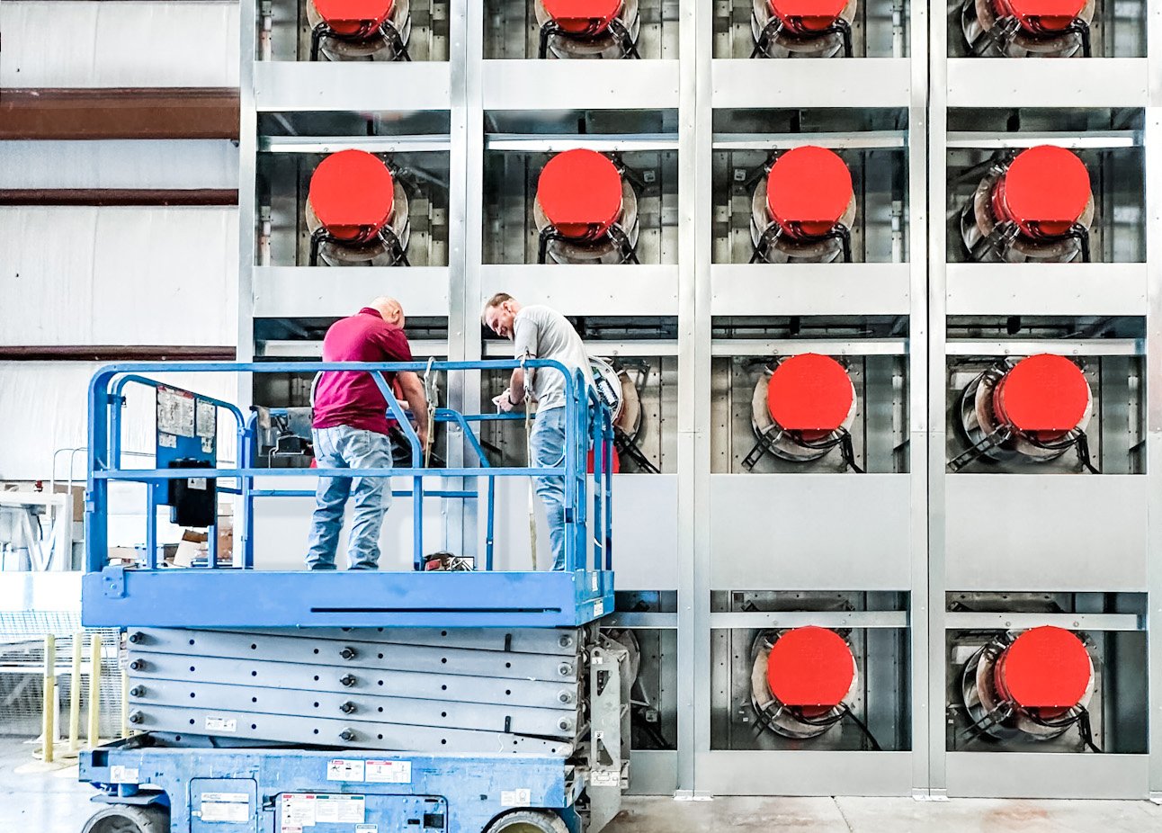 Some workers stand on a hydraulic lift in front of a data center..