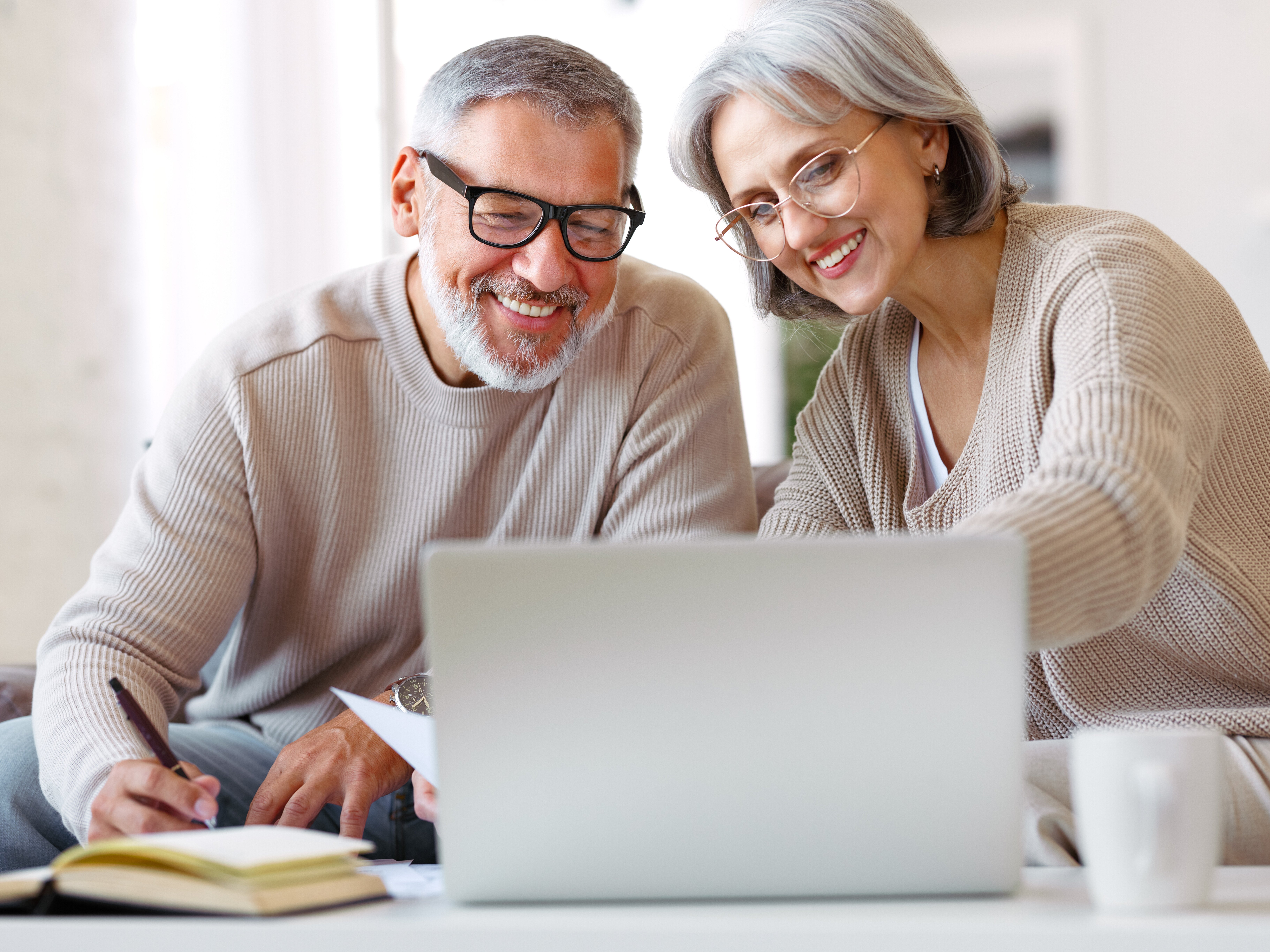 A smiling elderly couple searches through Medicare options on a laptop computer