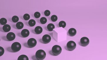 a pink cube standing amongst group of black spheres