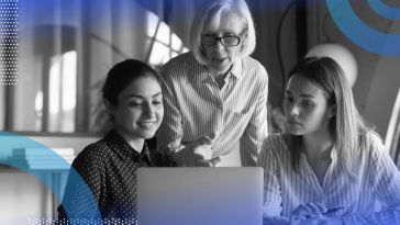 An older woman points something out on a computer screen to two younger women seated in front of her. /women-tech/5-advice-effective-stem-mentor