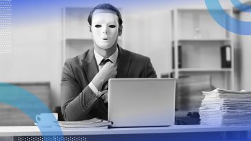 A man sits at a laptop with a mask on