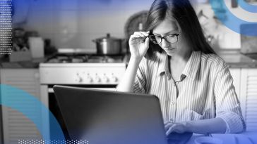 A woman looks at a laptop and adjusts her glasses