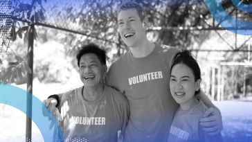 Three people with VOLUNTEER tshirts embrace and smile at the camera. /product-management/500-hours-volunteering-better-product-manager
