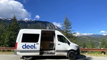 A white van with the blue Deel logo parked in front of a mountain.
