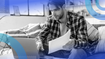 A young white man in a plaid shirt holds a document and types on a laptop. /product-management/must-document-no-code-low-code