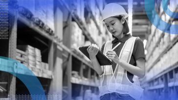A young woman in a warehouse, wearing a high-visibility vest and hard hat, checks something off on a tablet. /operations/benefits-for-every-employee
