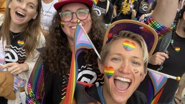 Evolve team members smile and celebrate at a Pride event. with rainbow attire and flags.