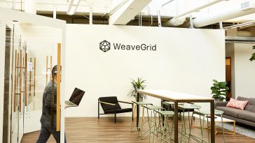 weavegrid's office with its logo on white walls and an open workspace. a man carrying a laptop. 