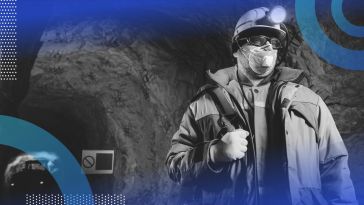 A miner wearing a mask and safety gear stands in an underground mine