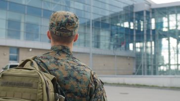 A service member in fatigues with his back to us walks toward a glass facaded building