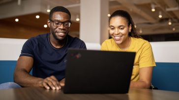A man and a woman smile at a laptop computer