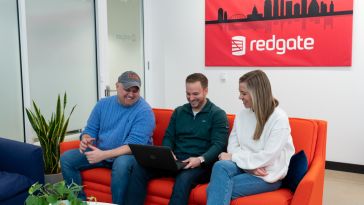 Three Redgate employees sitting on a red couch with a Redgate picture and logo behind them.