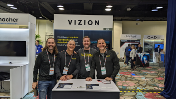Four of Vizion's team members in branded shirts and fleeces, standing together at a Vizion booth at a tech fair.