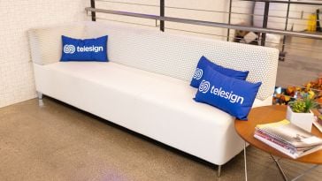 A white couch with several Telesign pillows on it.
