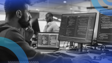 Image of a bearded man looking intently at three monitors with code on them.