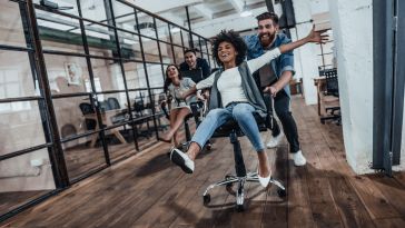 Coworkers racing wheeled chairs down an office hallway.