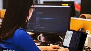 Photo of woman at laptop with separate monitor working on code