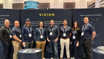 Eight of Vizion's team members posing for a photo in front of a black board with their name on top.