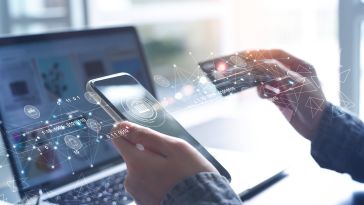 A pair of hands holding a phone and a credit card, in front of a laptop.
