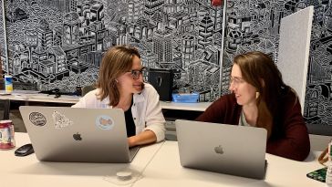 Two Cohere team members talking, smiling with laptops open