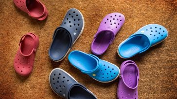 a variety of multicolored pairs of crocs on a jute rug