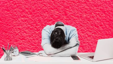 An employee lays their head down on their desk.