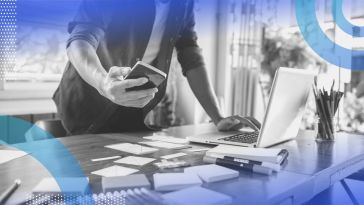 A UX designer looks at a smartphone at a desk covered with notes