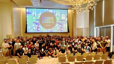 Large group photo of Huntress team inside a room with big screen overhead that says “Summer Summit 2022”