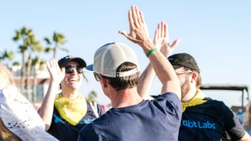 dbt Labs team members high-fiving outside with palm trees in the background.