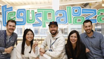 Group photo of five Tegus team members in front of sign reading “Teguspalooza.”