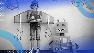 A child wearing cardboard wings and aviator goggles stands next to a smiling cardboard robot