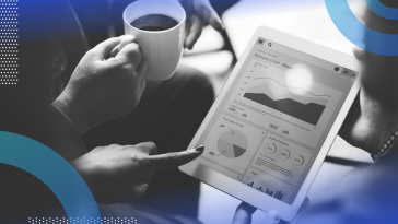 A tablet with various graphs is in the middle of a group of people. Only their hands are visible. Someone holds a cup of coffee.