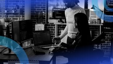 Two women work on code on a multiple monitor setup