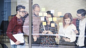 A group of coworkers look at sticky notes on a window.