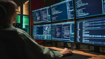 Cybersecurity worker looks at multiple screens of code.