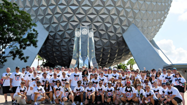 Large group photo of Kustomer team members wearing matching Mickey Mouse-themed t-shirts in front of the Epcot Center’s Spaceship Earth.