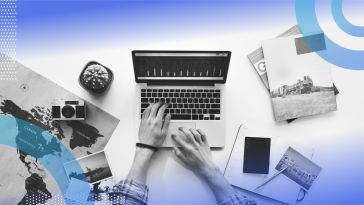 An aerial view of someone’s hands typing on a laptop surrounded by travel materials.