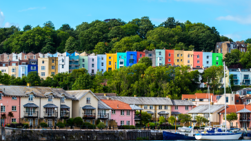 Landscape photo of Bristol featuring very colorful houses on the water, on a hill, as well s a boat on the water in the foreground..
