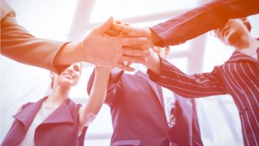 A team of professionals stacking their hands together in a gesture of unity.