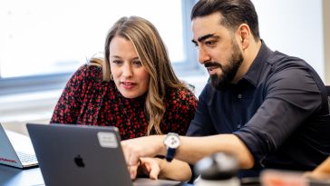 10Pearls team members Erin Mohideen and Armin Azarbad look at a laptop screen together.