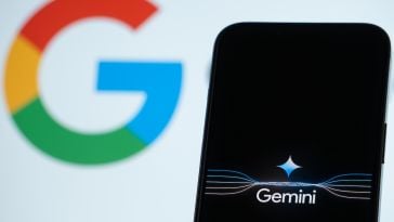 A smartphone with the word 'Gemini' on its screen, with the Google logo in the background. 