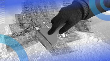 A close-up of a person’s hand scraping the ice off a car windshield.