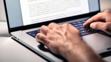 A close up of a pair of hands typing on a laptop keyboard.