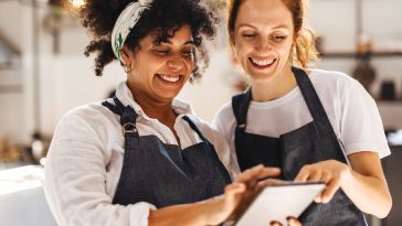 Two restaurant workers smile while interacting with a tablet.