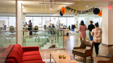 CarGurus office interior with employees milling about and a “Happy Halloween” banner hanging from the ceiling.